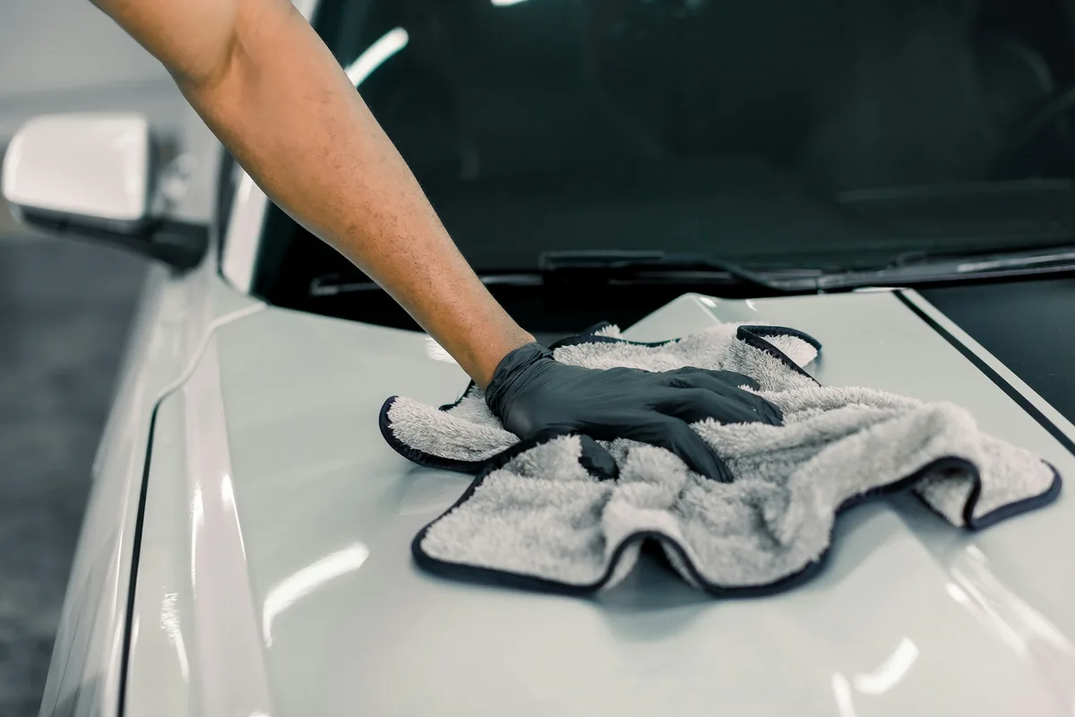 A gloved hand drying the hood of a white car with a microfibre towel.