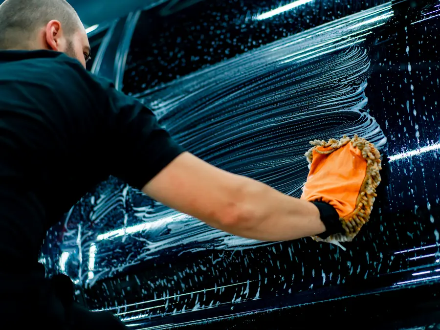 Hand washing a dark vehicle with foam and a wash mitt during a detail