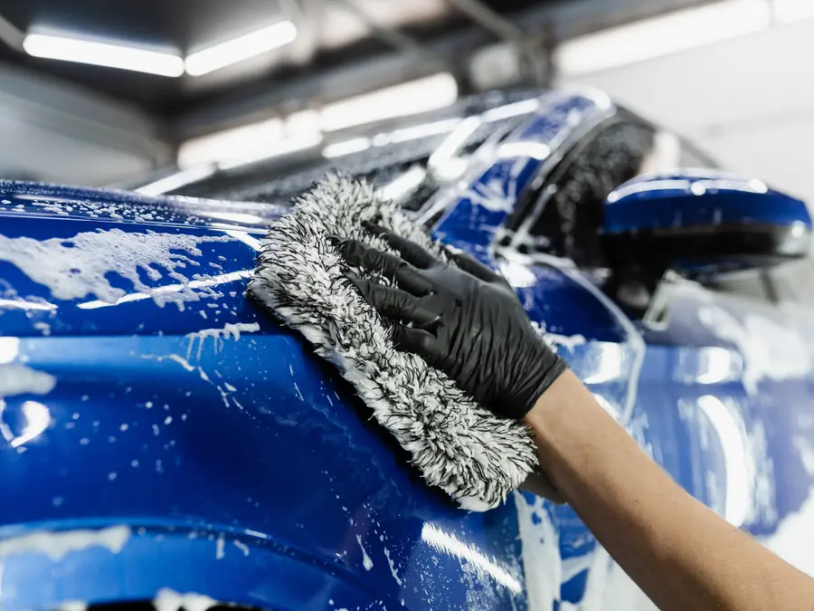 Hand washing a blue vehicle with foam during a maintenance visit